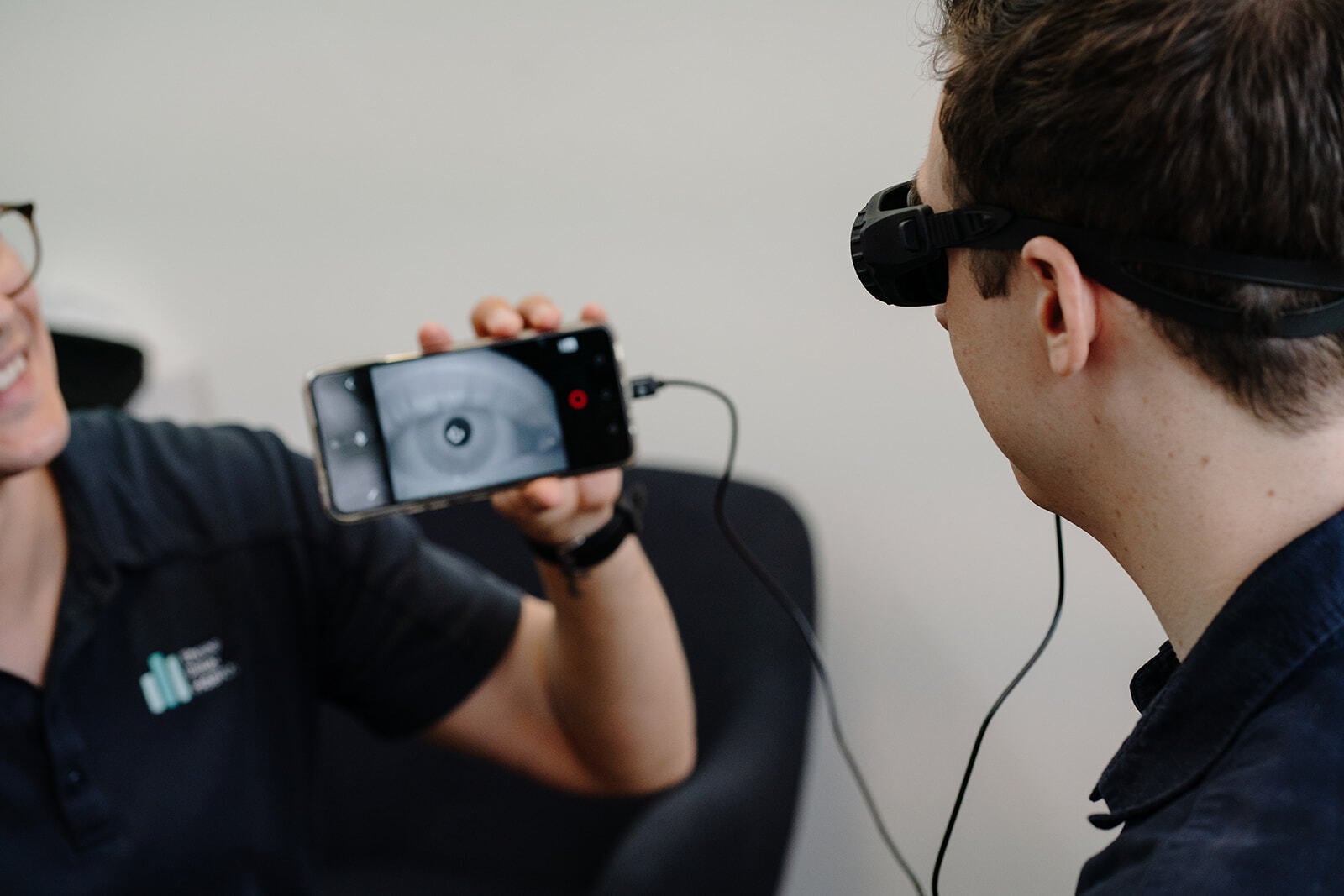 A physiotherapist holding up the Vesticam phone display while a patient wears the goggles