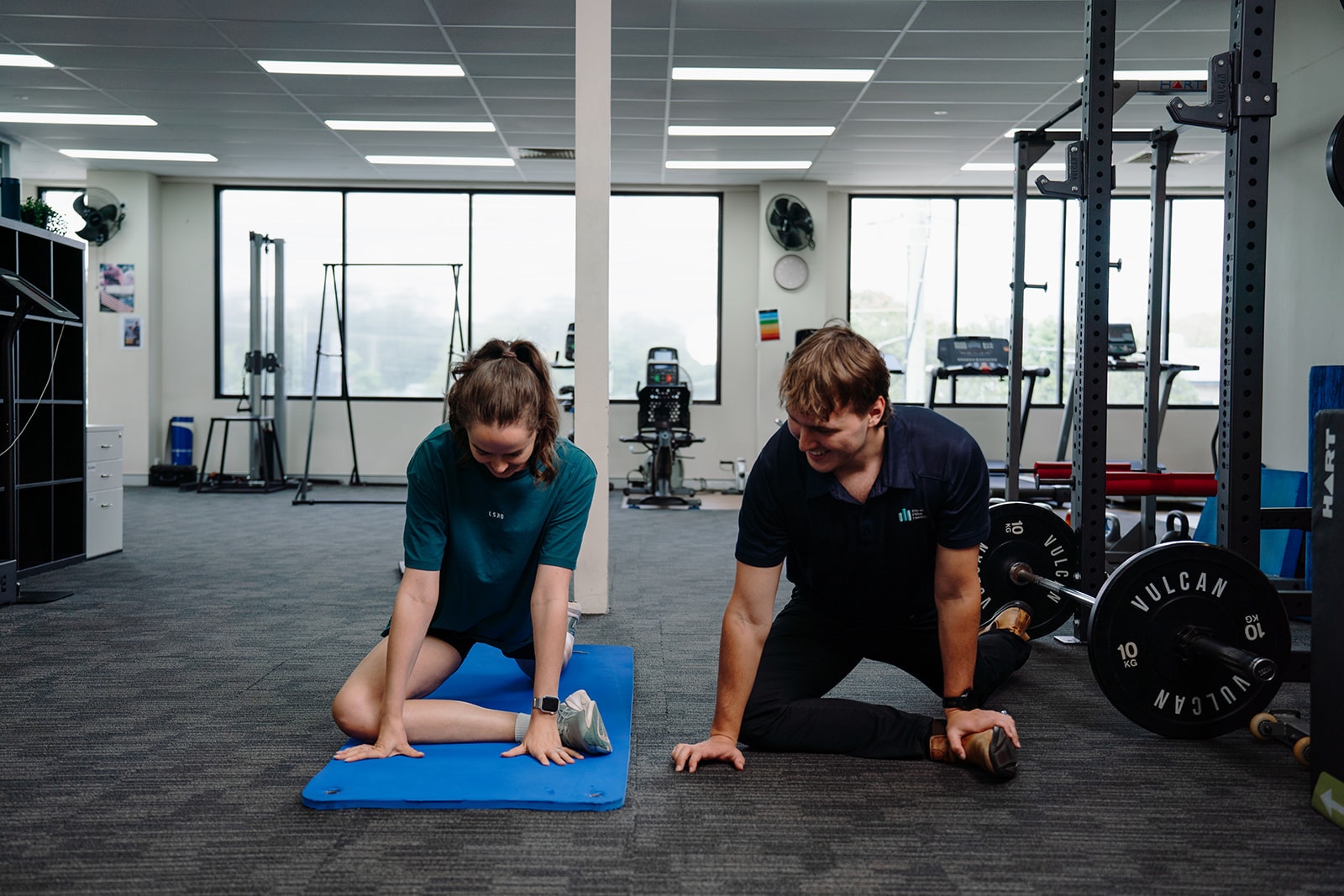 The gym at Three Pillar Health, Jarred kneeling next to a patient on the mat by the windows