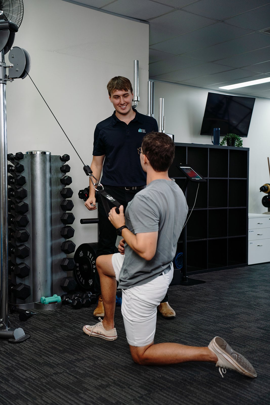 Jarred coaching a patient through a kneeling cable row, both smiling