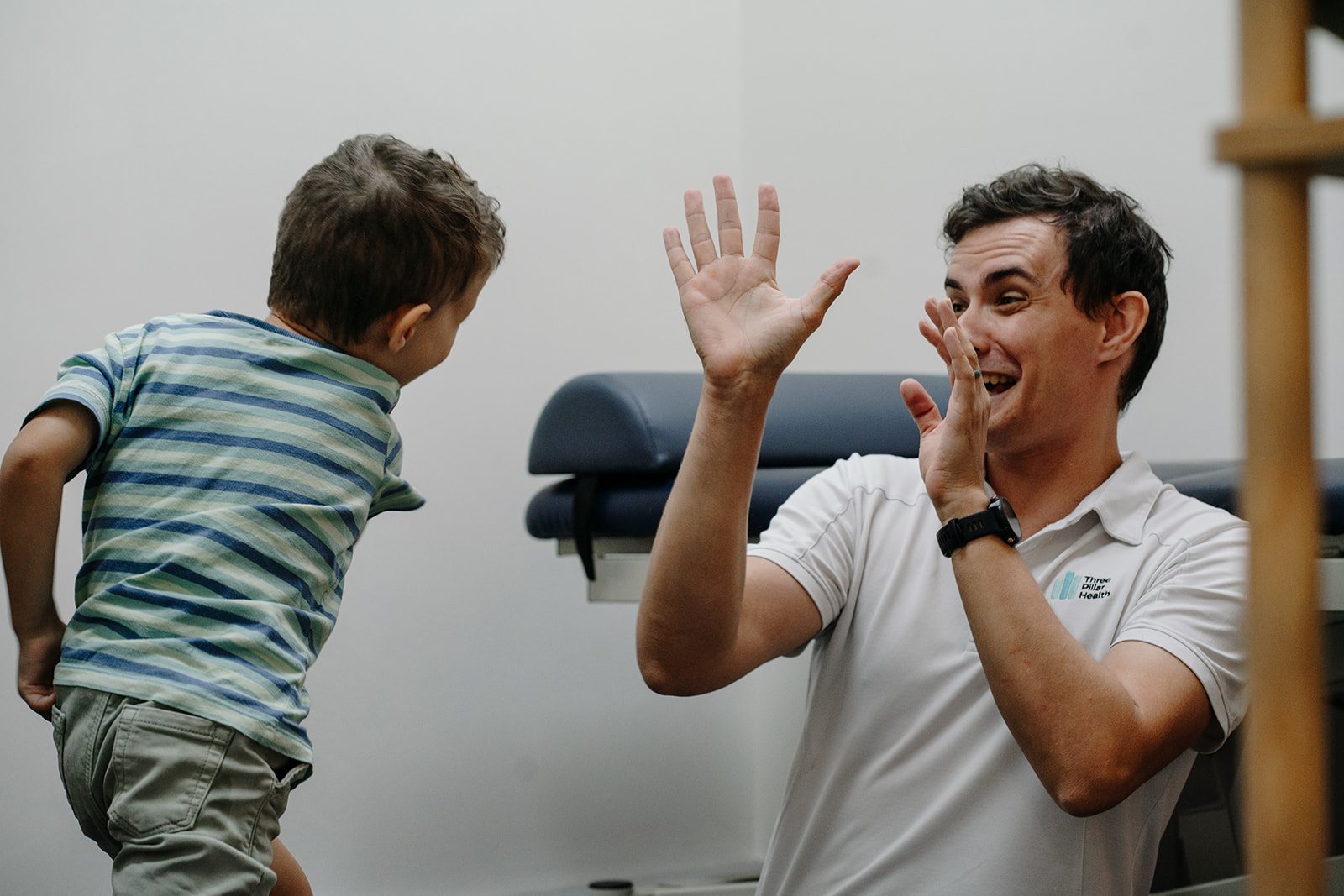 A young boy leaping towards speech pathologist Jonathon Cronk, who has his hands up in celebration