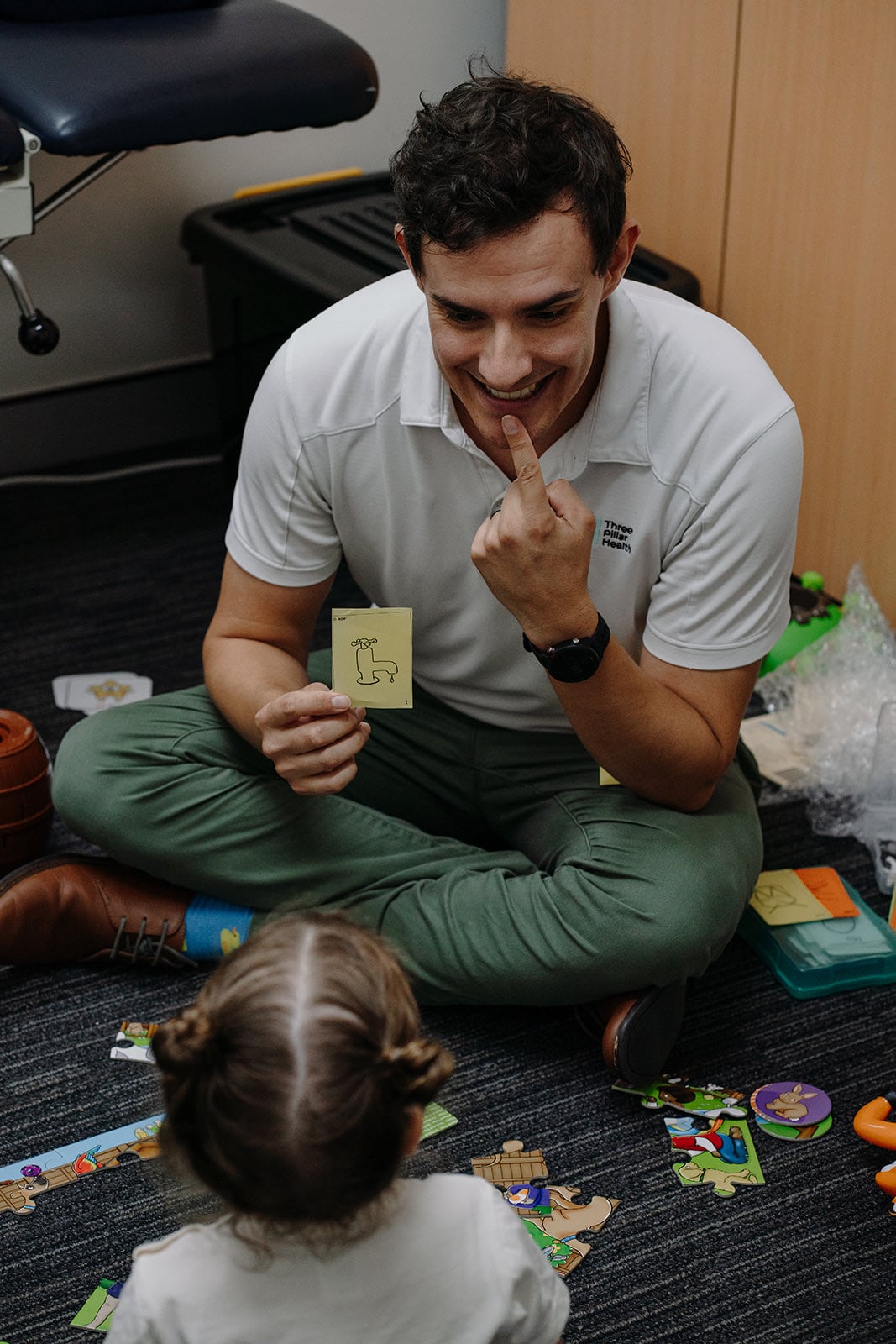 Speech pathologist Jonathon Cronk showing a picture card to a young girl sitting on the floor