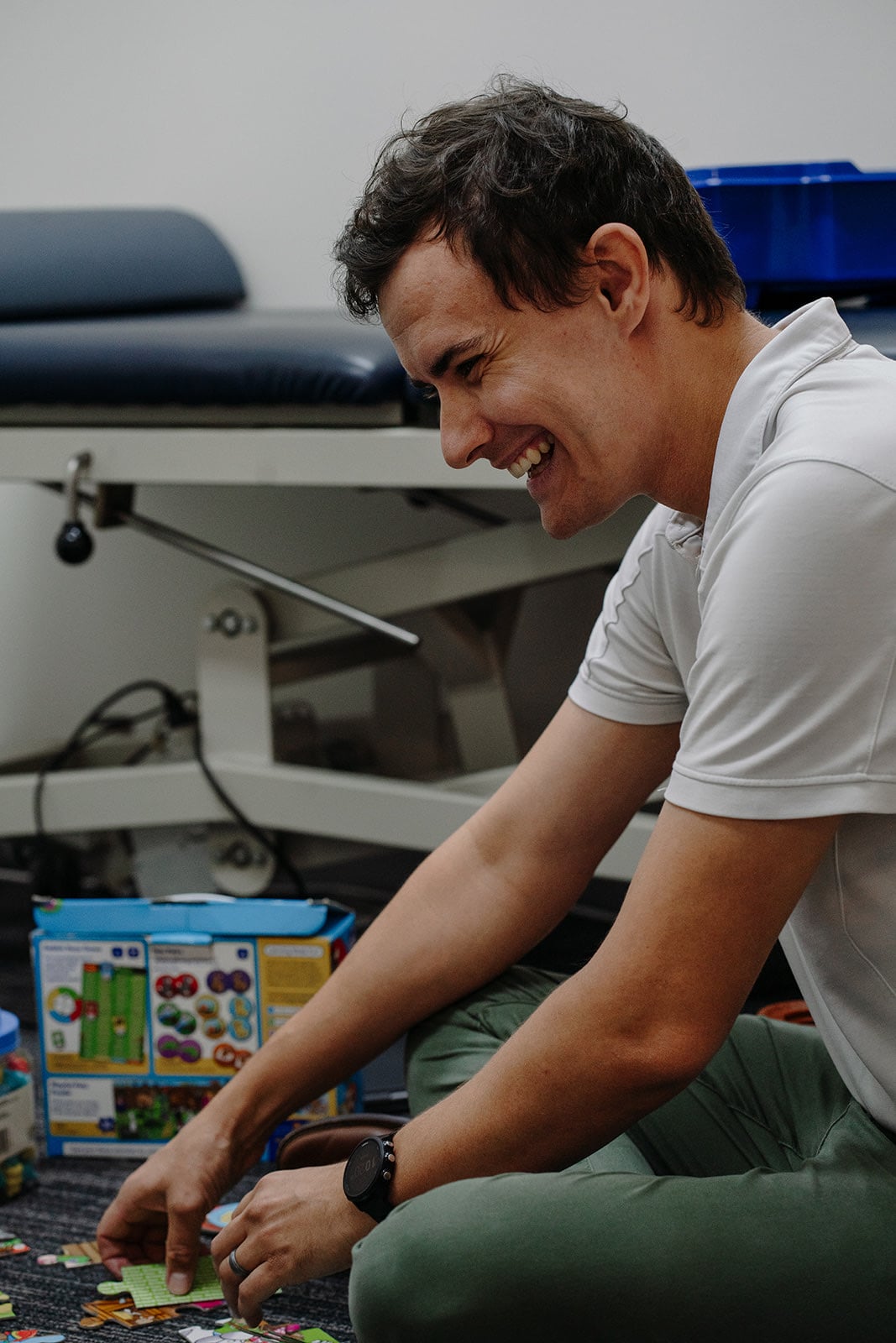 Speech pathologist Jonathon Cronk laughing while sitting on the floor beside a puzzle during a session