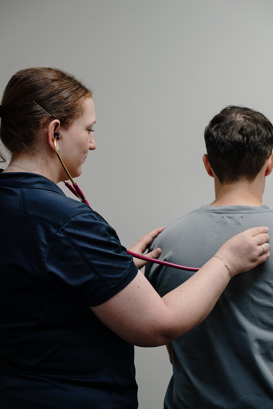 Kylie listening to a patient's breathing through a stethoscope on their back