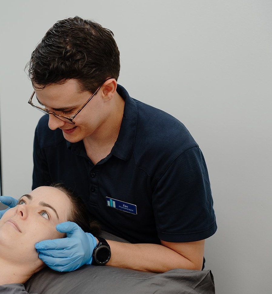 Physiotherapist Zac Cronk treating a patient's jaw, gloved hands either side of the jaw